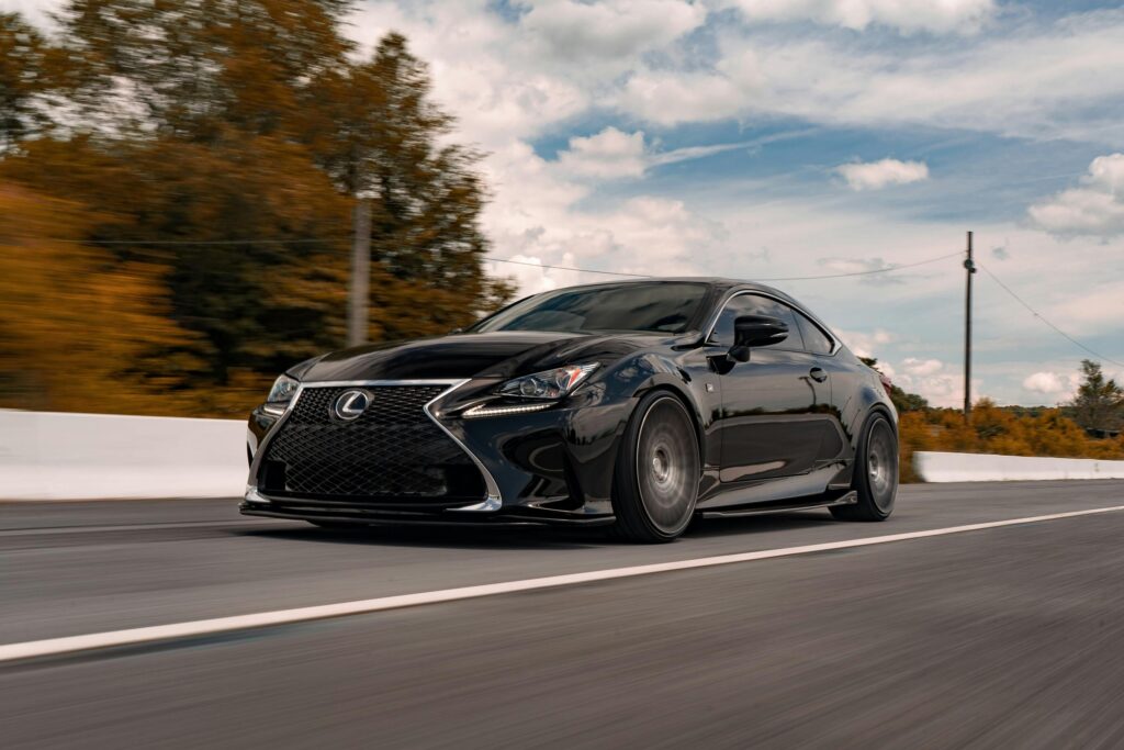 A black luxury car driving swiftly on an open road amidst scenic landscapes and clear skies.